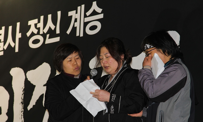 故 김재기 열사의 부인이 결의대회 참가자들에게 하고 싶은 말을 토해내다가 솟구치는 눈물을 참고 있다.