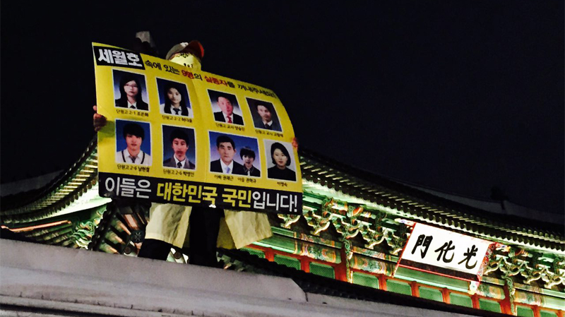 세월호 희생자 가족이 광화문 누각 앞 경찰 차벽에 올라가 피켓 시위를 하고 있다.