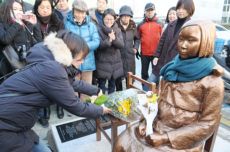 지난해 12월 30일, 일본 국기가 올려다 보이는 부산시 동구 주부산일본국총영사관 앞에 평화의 소녀상이 재설치 되어 있다. 소녀상에 꽃다발을 전하고 있는 시민들.