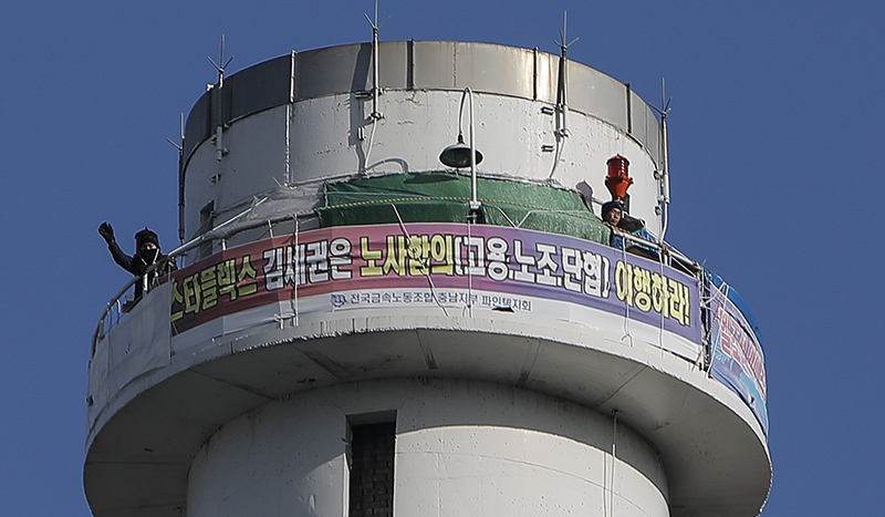 스타플렉스(파인텍) 투쟁 승리를 위한 공동행동 회원들이 지난 10일 오전 서울 양천구 서울에너지공사에서 공장 정상화, 단체협약 이행 등을 촉구하며 스타플렉스 서울사무소를 향해 오체투지 행진을 한 가운데 금속노조 파인텍지회 홍기탁 전 지회장(왼쪽), 박준호 사무장이 굴뚝에서 손을 흔들고 있다.