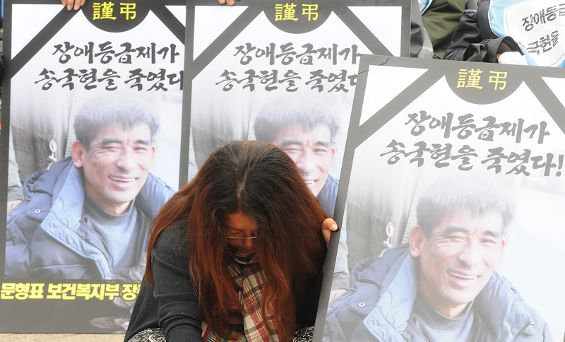 2014년 서울 시청광장에서 열린 '장애등급제 희생자 故 송국현 동지 장애인장'에서 참가자들이 송국현 씨를 추모하는 피켓을 들고 있다.