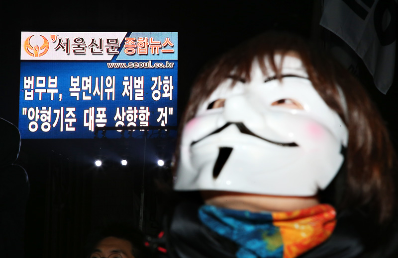 28일 오후 서울 중구 파이낸스센터 앞에서 열린 백남기 농민 쾌유 기원 경찰청장 파면 물대포 추방 시민대회에서 복면을 쓴 참가자 뒤로 정부가 복면시위 처벌을 강화한다는 뉴스가 보여지고 있다.
