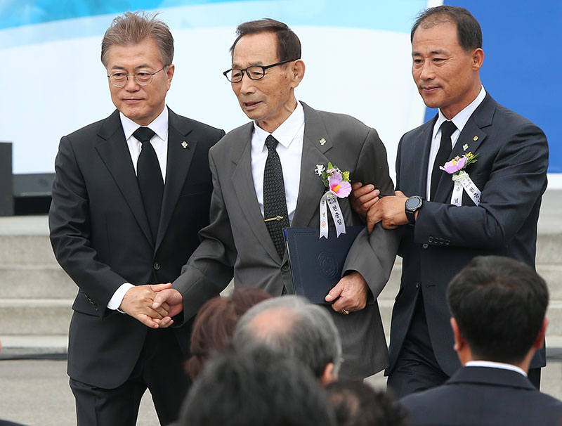 문재인 대통령이 6일 오전 서울 동작구 국립서울현충원에서 열린 제62회 현충일 추념식에서 국가유공자인 박용규(가운데) 씨를 부축하며 자리로 이동하고 있다.