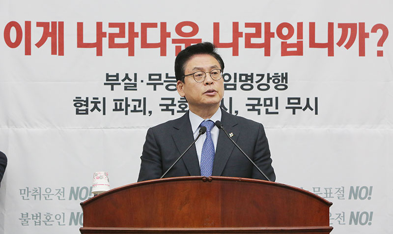 자유한국당 정우택 원내대표가 19일 오전 국회에서 열린 자유한국당 의원총회에서 발언하는 가운데 '이게 나라다운 나라입니까?'라고 적힌 현수막이 보이고 있다.