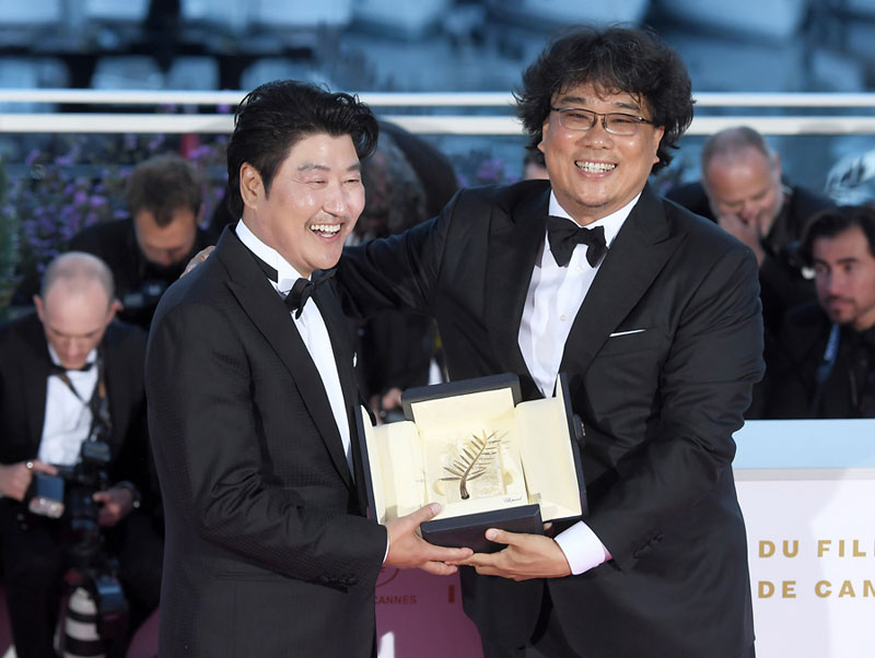 제72회 칸 영화제에서 황금종려상을 수상한 영화 '기생충'의 배우 송강호와 봉준호 감독(오른쪽)이 기자회견장에서 트로피를 안고 함박웃음을 짓고 있다.