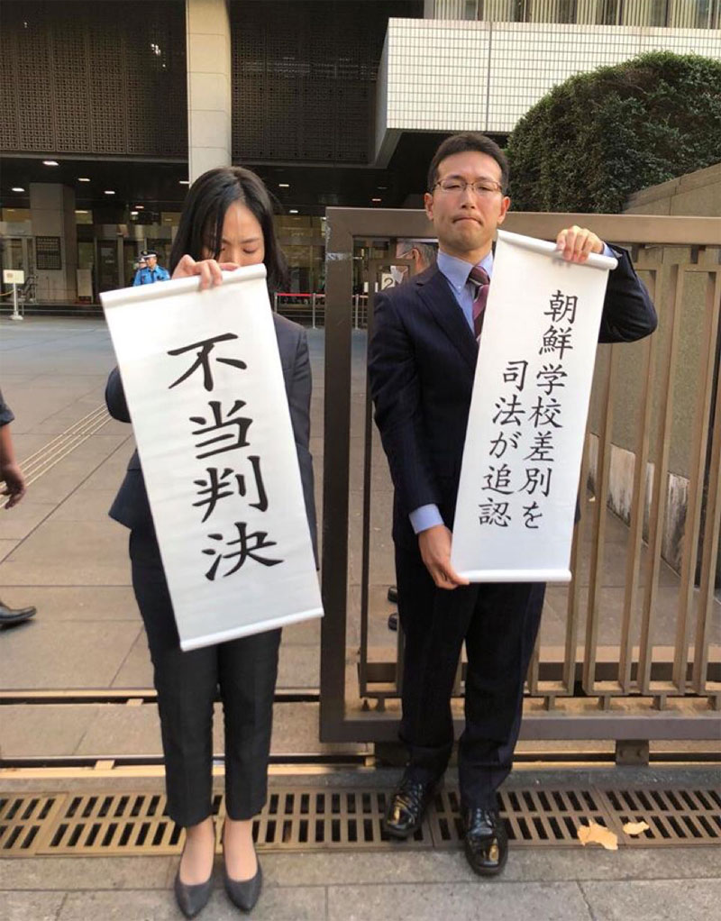 일본 도쿄의 조선중고급학교의 졸업생이 일본 정부가 고등학교 무상화 대상에서 조선학교를 제외한 것은 위법이라며 제기한 소송의 항소심에서 패소했다. 판결 후 조선학교 측 변호인들이 비통한 표정으로 부당판결이라는 글귀를 내보이고 있다.<br